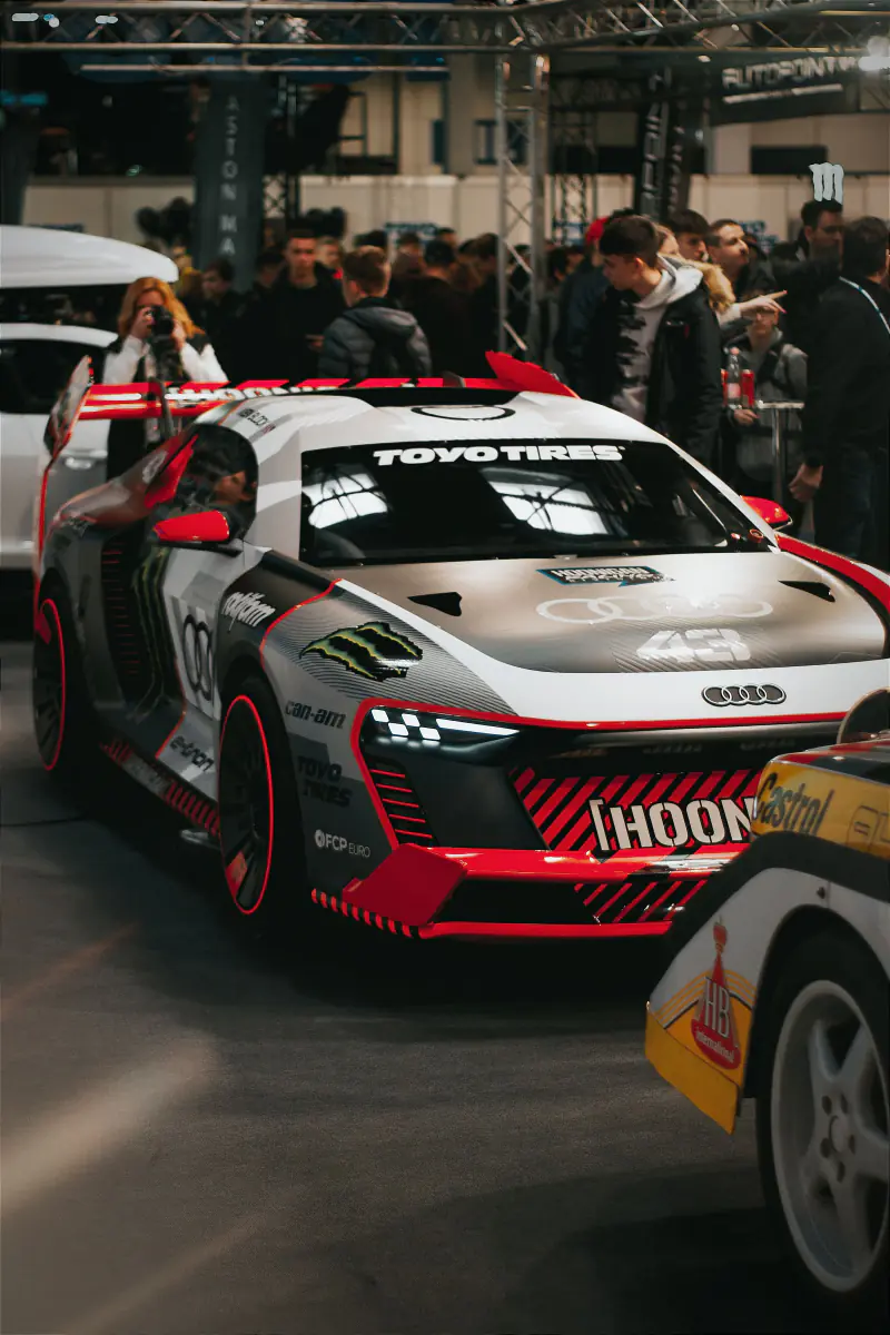 Audi-racerbil med røde detaljer omgivet af tilskuere på en messe